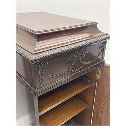 Pair early 20th century Hepplewhite style mahogany pedestal cabinets, cavetto moulded top with foliate carved edge over secret frieze drawer with applied trailing floral and ribbon decoration, each with button release underneath, oval panelled door with trailing harebell and central flower head motif decoration enclosing shelves, fitted cutlery drawer and lined cellarette drawer, on turned acanthus carved feet