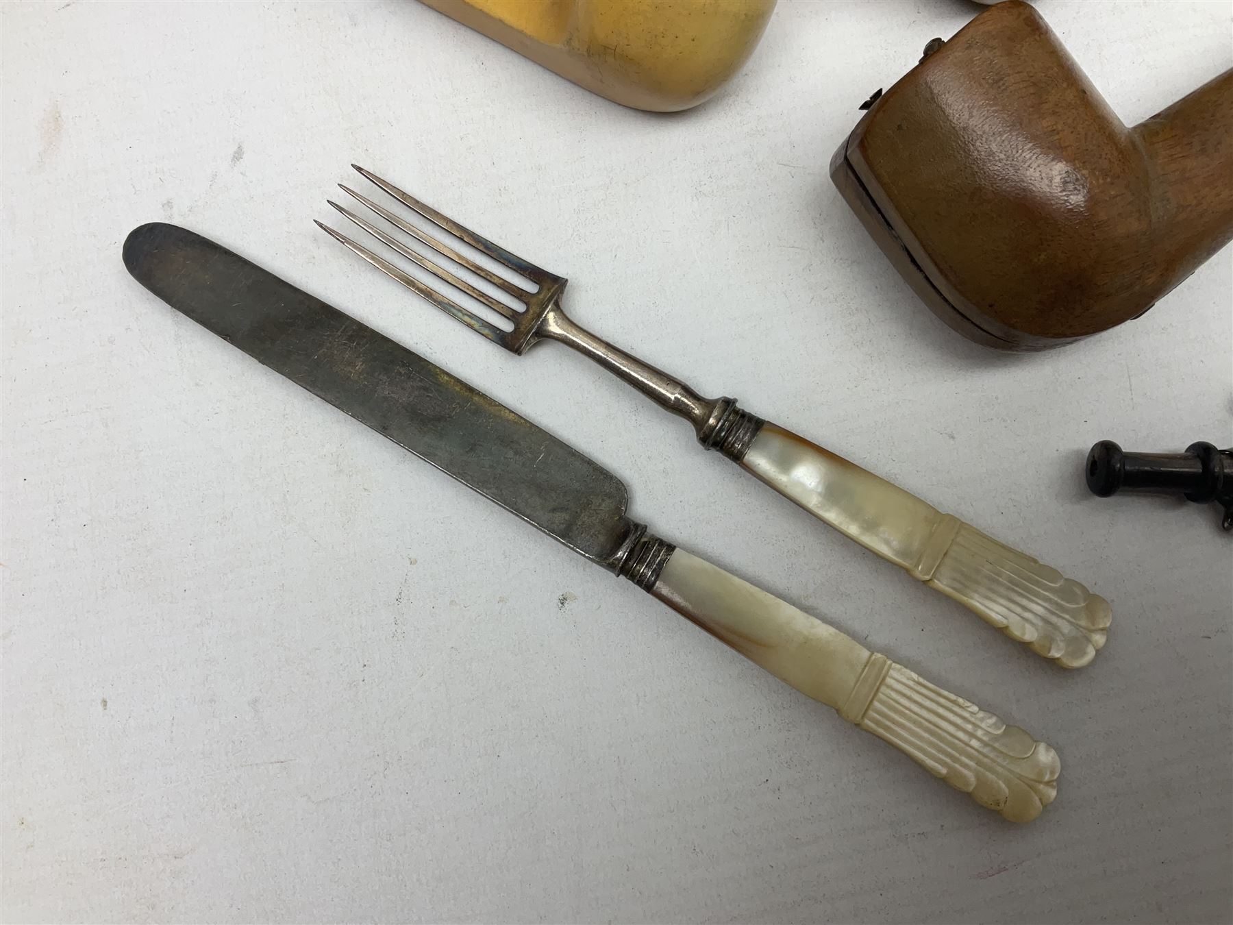 Swiss mountain hunters tobacco pipe with a horn mouthpiece, metal hinged pierced lid and brass chain, the black coated body adorned with small metal cow flowers, together with two other pipes and case, brass mounted horn, brass mounted bone box, carved mother of pearl handled knife and fork and brass jug