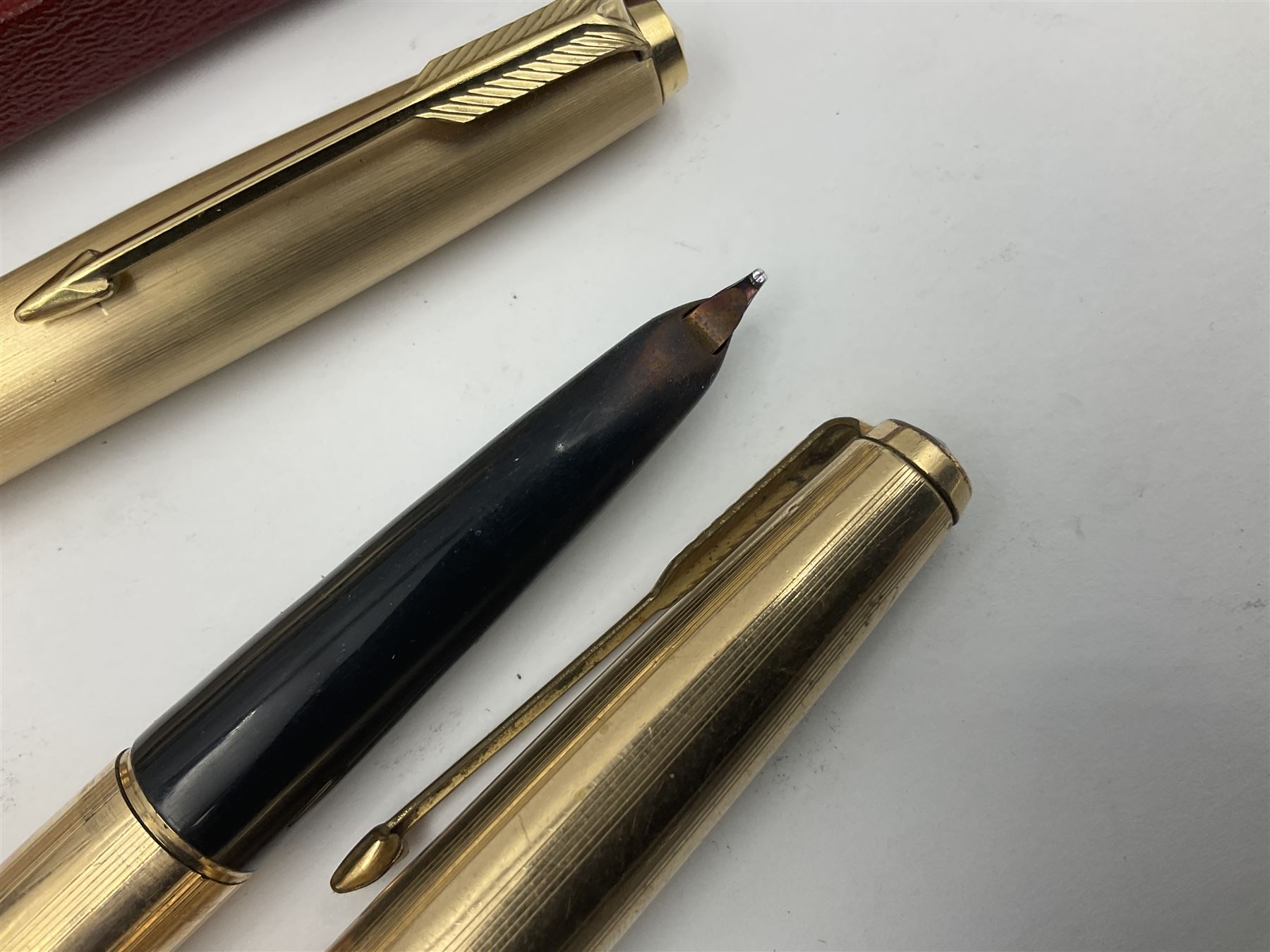 Three rolled gold Parker fountain pens, comprising an example with a gold nib marked 14K 585 and barrel with a shell stamp, a Parker 61 fountain pen with inset gold arrow to the nib, and another similar, all with striated decoration and arrow clips to the caps, L13cm, one with box