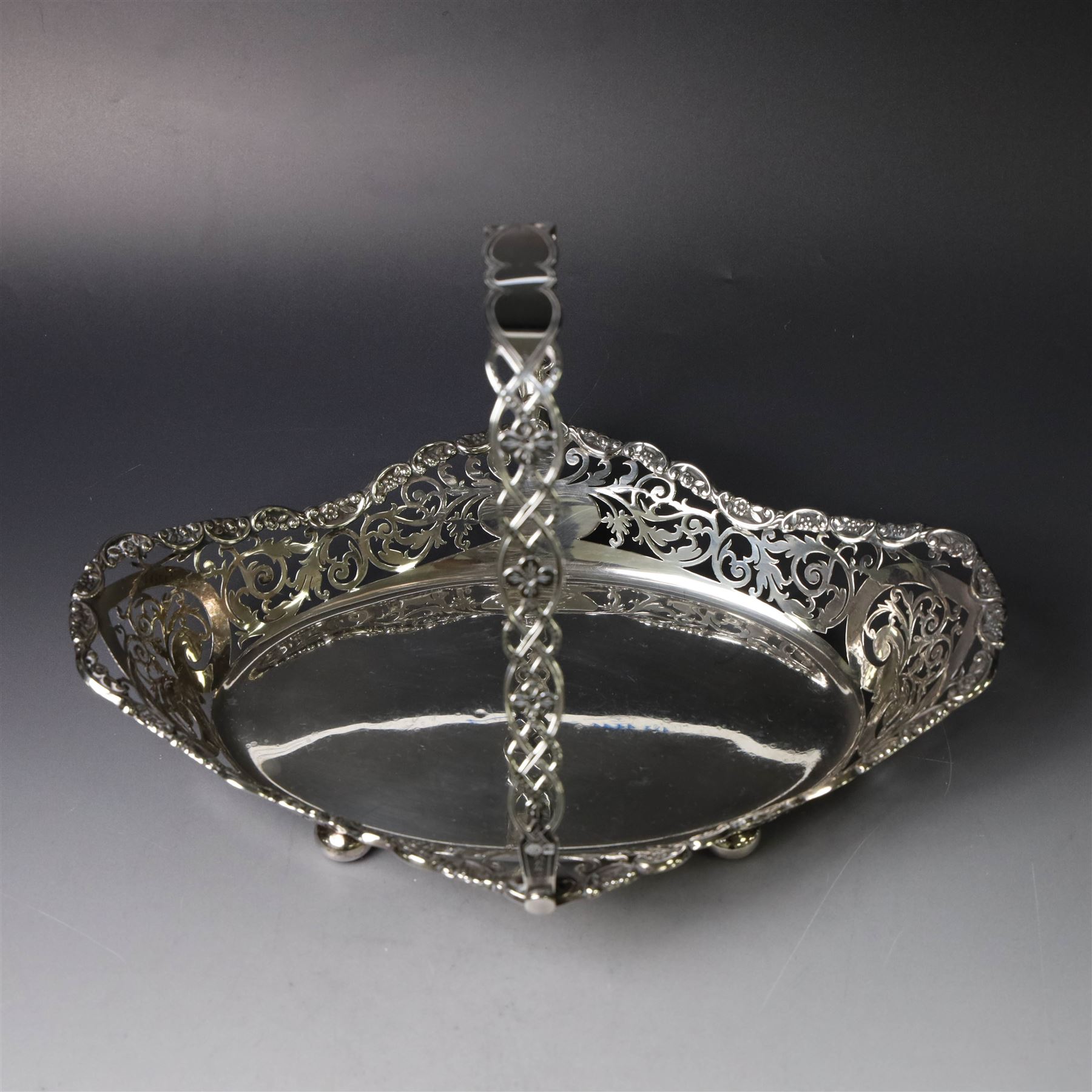 Early 20th century swing handled basket, of oval form with pierced sides and floral C scroll rim, upon four bun feet, hallmarked William Hutton & Sons Ltd, Sheffield 1915, widest point W29cm