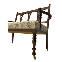 Edwardian walnut two seat salon settee, triple pierced splat back, sprung seat upholstered in floral striped fabric, turned front supports with brass castors