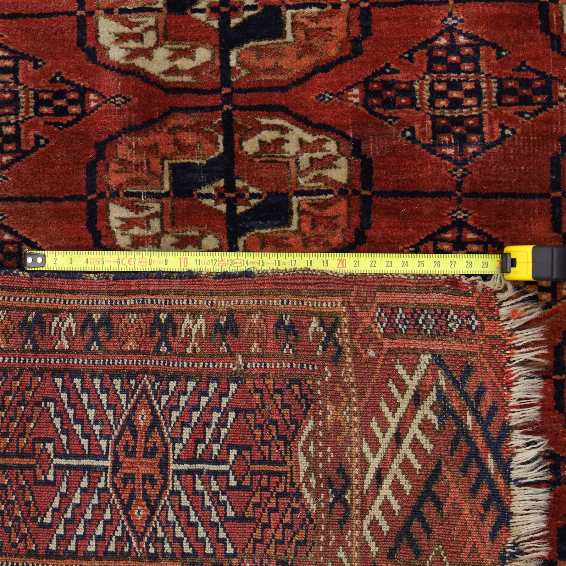 Central Asian Turkmen Tekke hand-knotted rug, madder red field decorated with rows of octagonal guls linked by secondary motifs within a dense geometric border, with fringe ends  