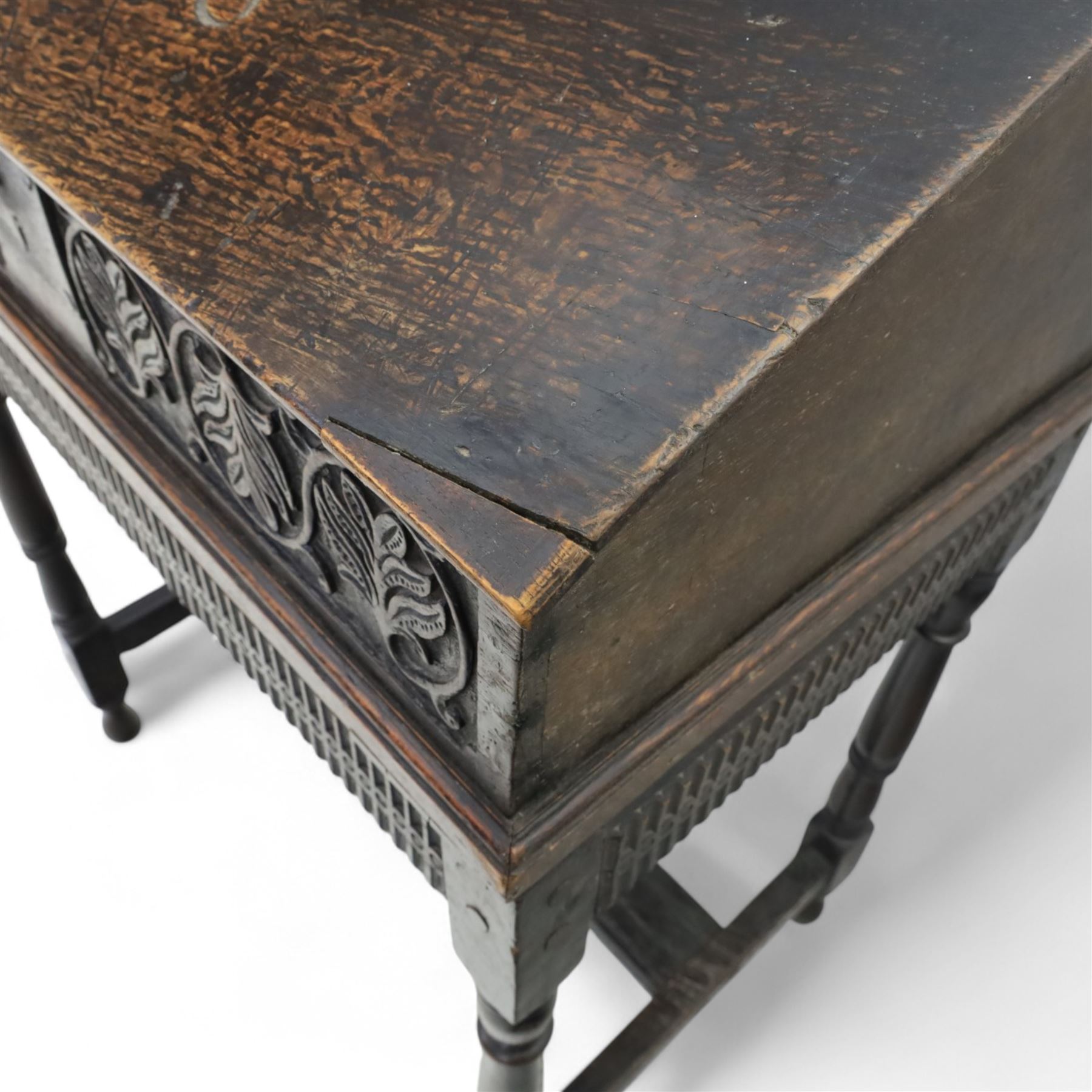 18th century carved oak Bible box on stand, the sloping lid with incised initials ‘MD’ and iron strap hinges, the front carved with stylised leaf and scroll panels enclosing central iron lockplate, on stand with gadrooned frieze, turned legs and plain stretchers