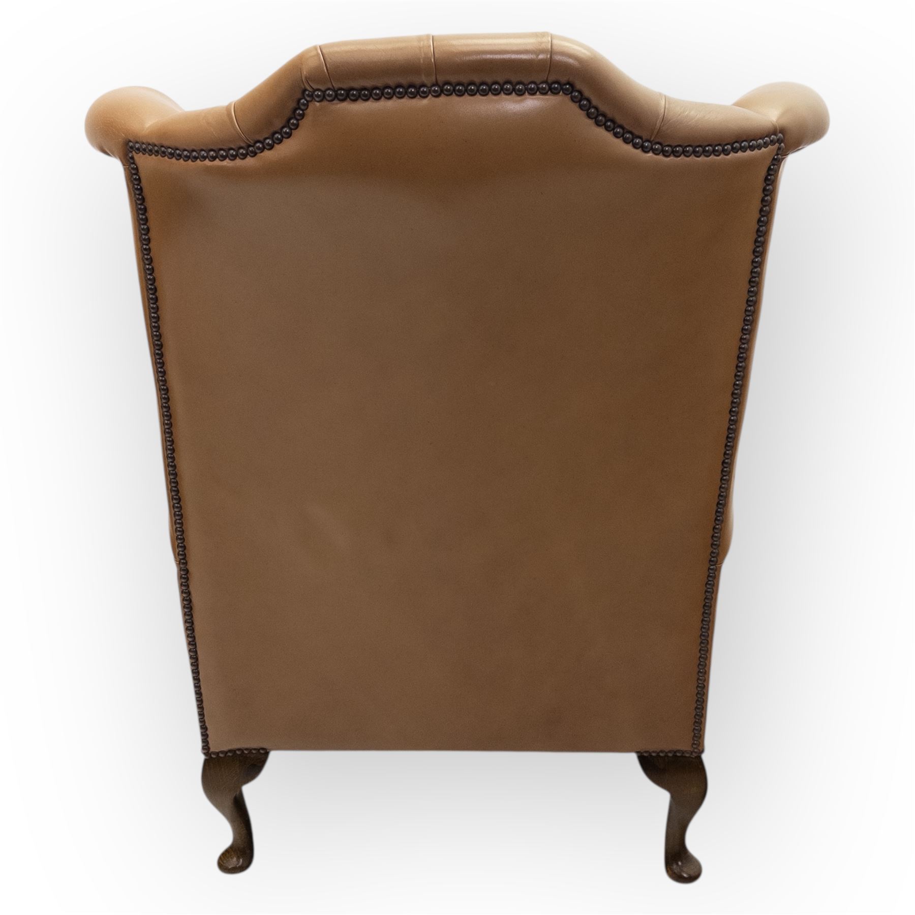 Contemporary set of two tan leather armchairs, comprising a deep-buttoned chesterfield and a matching wingback chair, both with rolled arms, studded borders