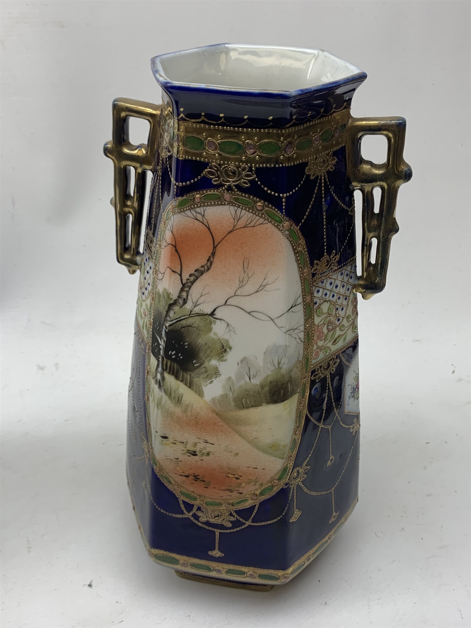 A pair of Japanese Nippon Kinjo vases, of tapering hexagonal form with twin stylised handles, the cobalt blue ground with oval hand painted panels to front and verso depicting landscapes, further detailed with smaller floral bands and panels and heightened with gilt, each with mark beneath, H30.5cm.  
