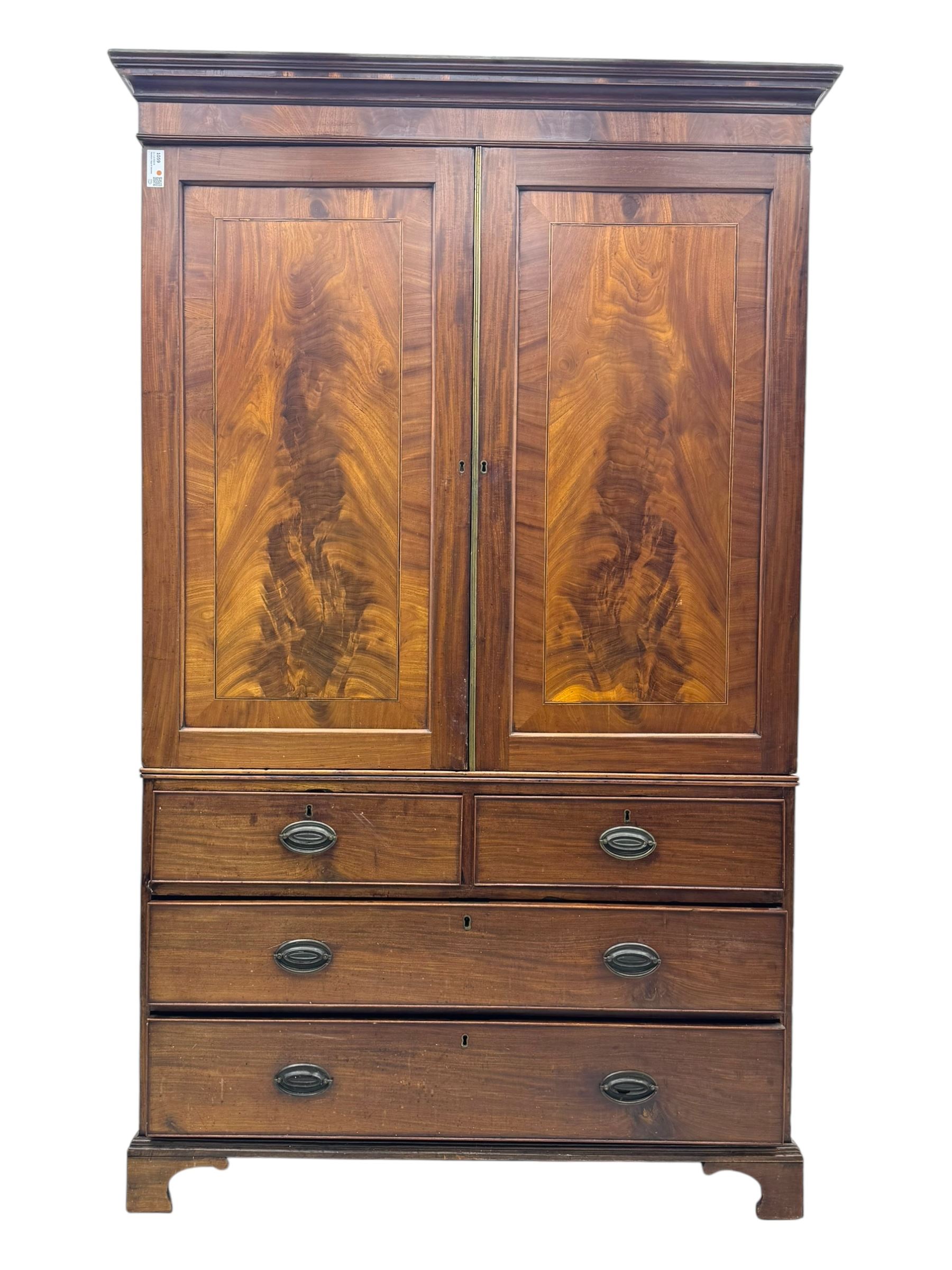 Early 19th century mahogany linen press cupboard, projecting moulded cornice over figured frieze, two panelled doors enclosing shelves, fitted with two short and two long cock-beaded drawers, on bracket feet 