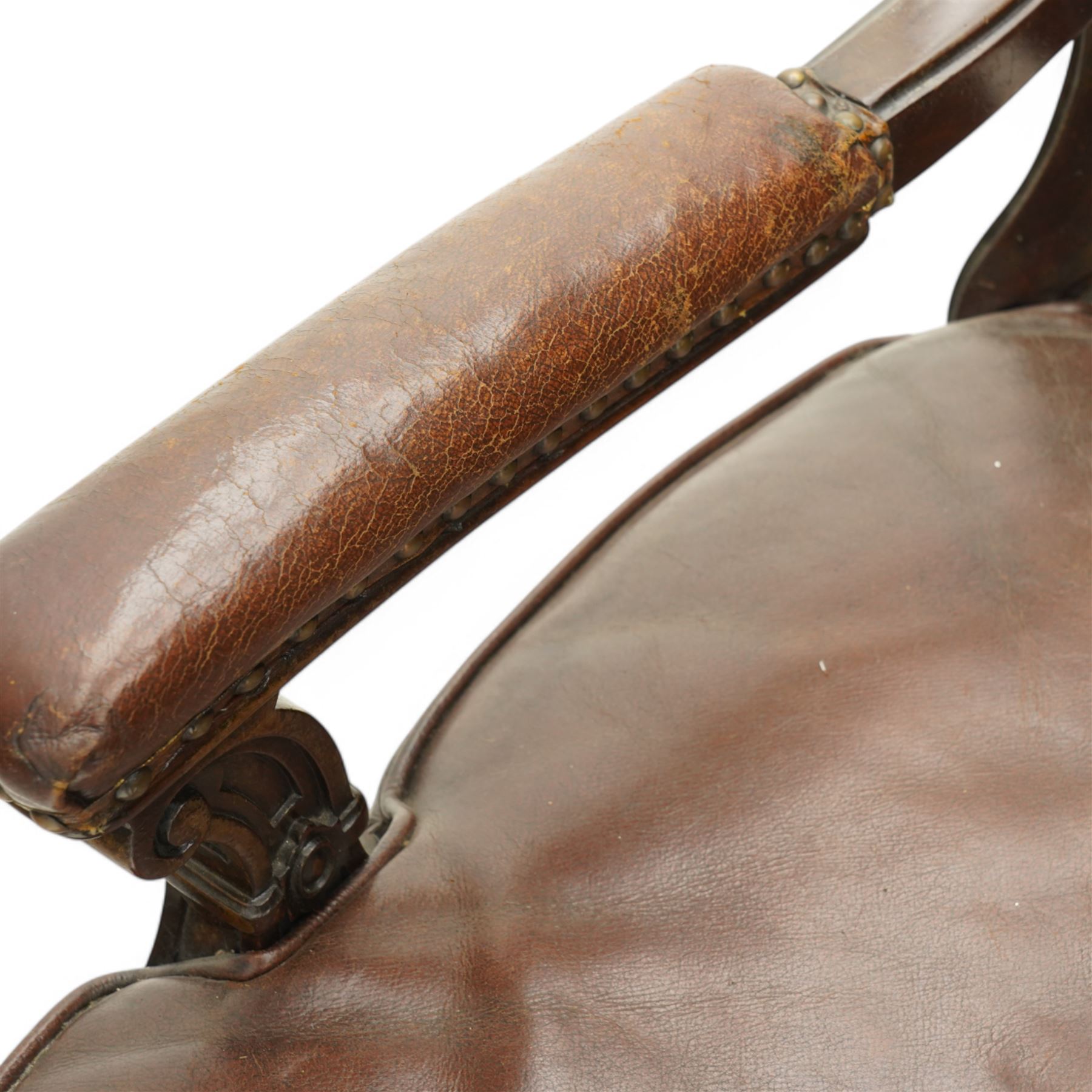 Victorian mahogany library elbow chair, arched cresting rail over shaped and pierced splat carved with cartouche, upholstered arms and seat in brown leather with studded bands, turned and lobe carved front supports on brass and ceramic castors 
