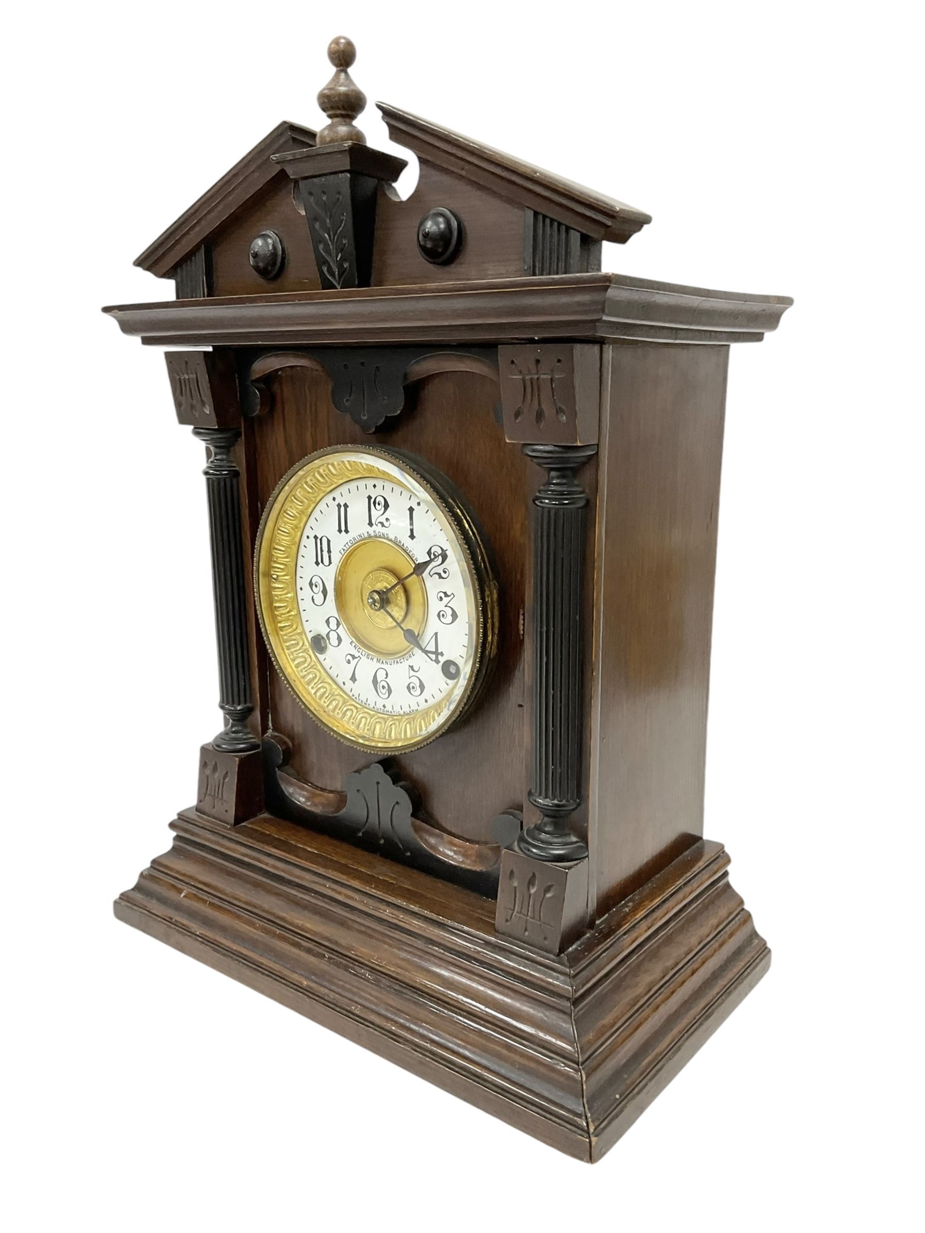Fattorini of Bradford - oak cased early 20th century mantle clock with alarm, rectangular case with a broken pediment, turned finial and matching carved pilasters to the front, on a broad stepped plinth with a flat base, circular dial with an ivorine chapter within a decorative gilt bezel, Arabic numerals , spade hands and alarm setting disc to the centre, two train spring driven movement striking a coiled gong and bell. With key and pendulum. 
