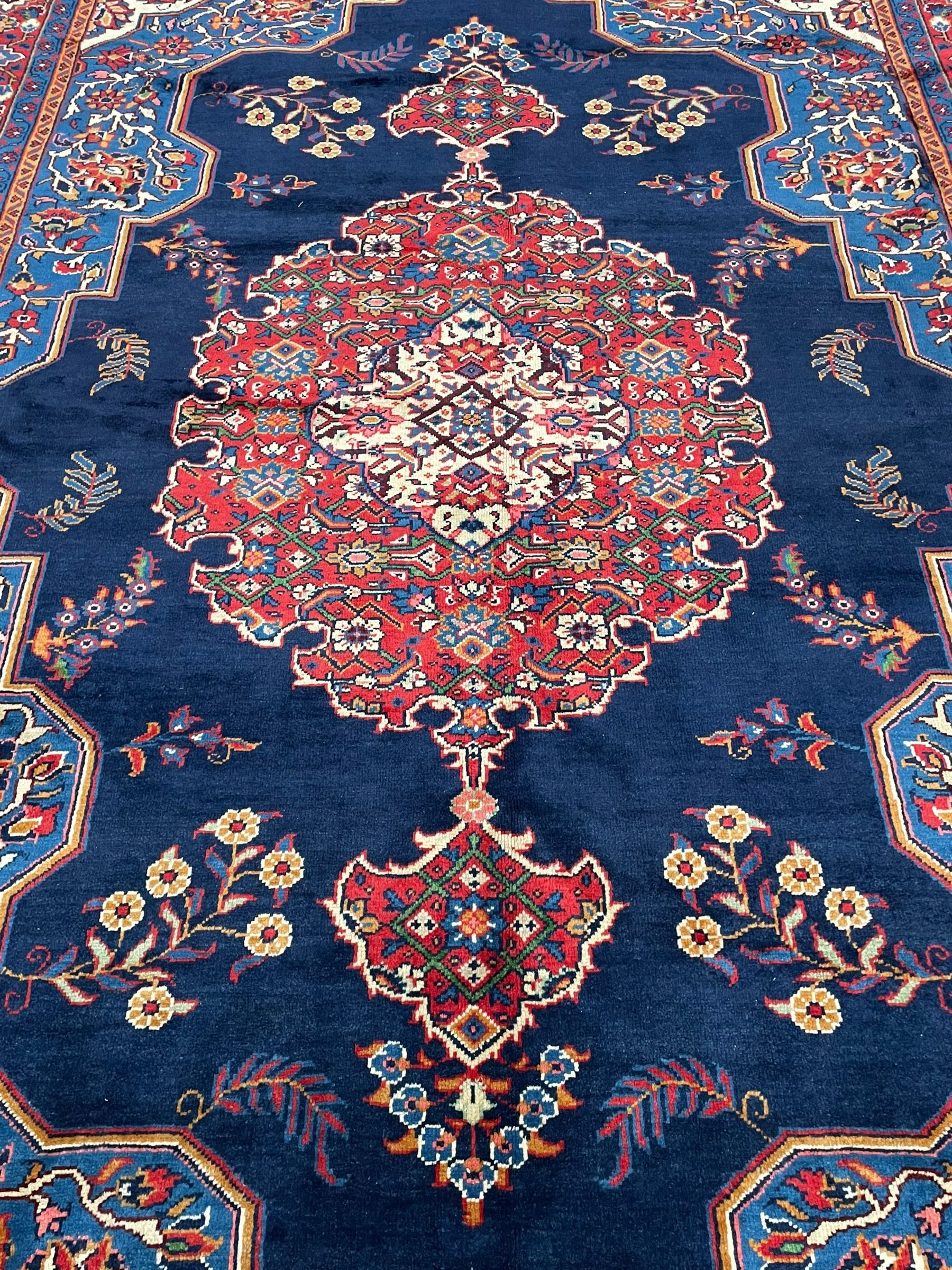 Persian Veis indigo ground carpet, the field with large pole medallion decorated with Herati motifs and surrounded by floral sprays, crimson ground border with repeating cross motifs and stylised flower heads, within guard stripes 