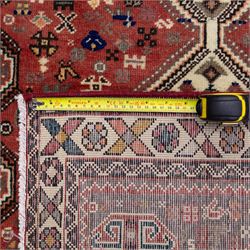 South West Persian Abadeh hand-knotted runner, madder red field decorated with a vertical sequence of stepped lozenge medallions, each enclosing stylized geometric motifs and angular devices, surrounding field filled with tribal symbols and abstract forms, enclosed within a narrow main border and flanked by multiple guard stripes, with fringe ends 