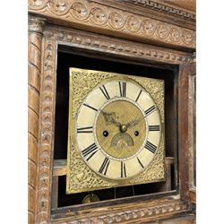 19th century carved oak longcase clock, projecting cornice over guilloche carved frieze, square brass dial with silvered Roman chapter ring and calendar aperture, decorated with ornate mask cast spandrels, the trunk door and base carved with potted plant, twin train driven eight day movement striking on bell