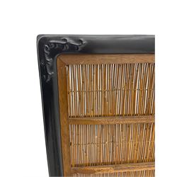 Chinese ebonised hardwood and reed work screen, with carved scroll decoration to corners, on block sledge feet