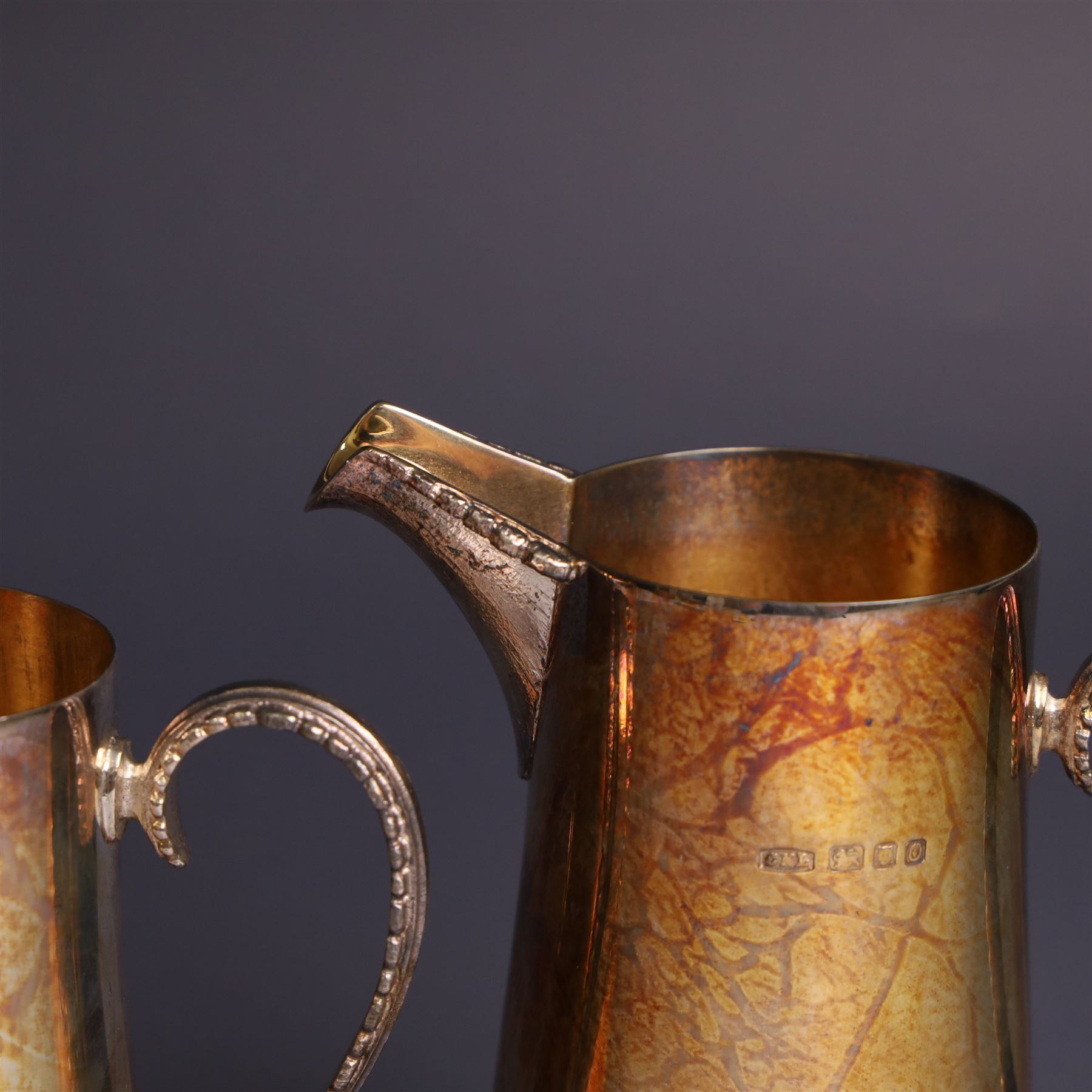 Two graduating silver milk jugs, each of tapering cylindrical form, with engraved central cartouche to body and upon three paw feet, hallmarked Christopher Nigel Lawrence, London 1988, tallest H13cm