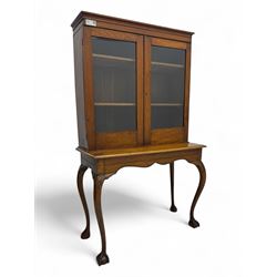 Late 19th century oak display cabinet, rectangular form with a pair of glazed doors enclosing shelves, raised on cabriole supports with carved detailing ending in claw feet