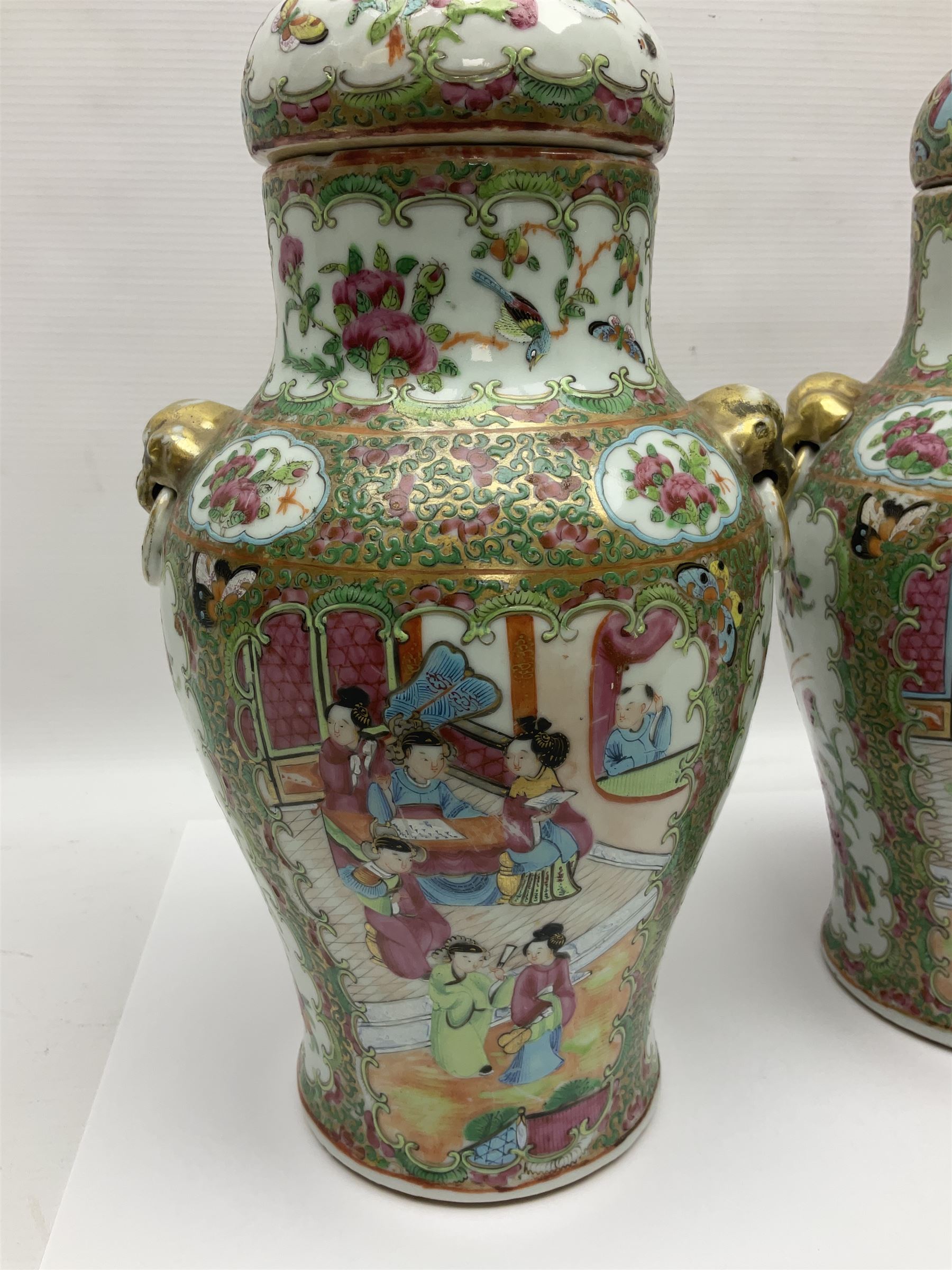 Pair of 19th century Chinese Famille Rose vases and covers, each of baluster form with twin gilt lion mask ring handles to shoulders, the flattened domed covers with gilt temple lion finials, each decorated with alternating reserves of bijin and attendants, and birds and butterflies amongst blossoming peonies, against a gilt ground profusely decorated with stylised scrolls, H32.5cm