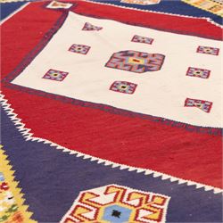 South West Persian Qashqai kilim, woven in flatweave with tones of indigo blue, madder red, yellow, turquoise, and green, with a bold central diamond medallion on an ivory ground, enclosing smaller lozenge motifs and flanked by deep madder red panels, field framed by a broad indigo border with polychrome geometric devices and serrated motifs 