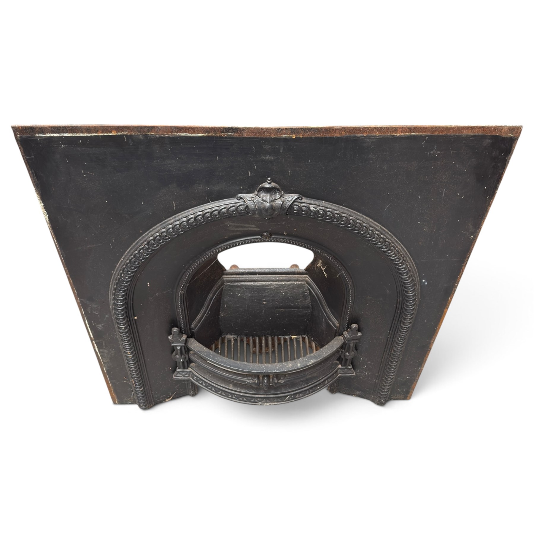 Late Victorian black-painted cast iron fireplace, the arched surround with anthemion cartouche and guilloche-moulded border, enclosing a bow-front fire basket with finialled standards, railed front and leaf-cast apron, with sheet-metal backplate