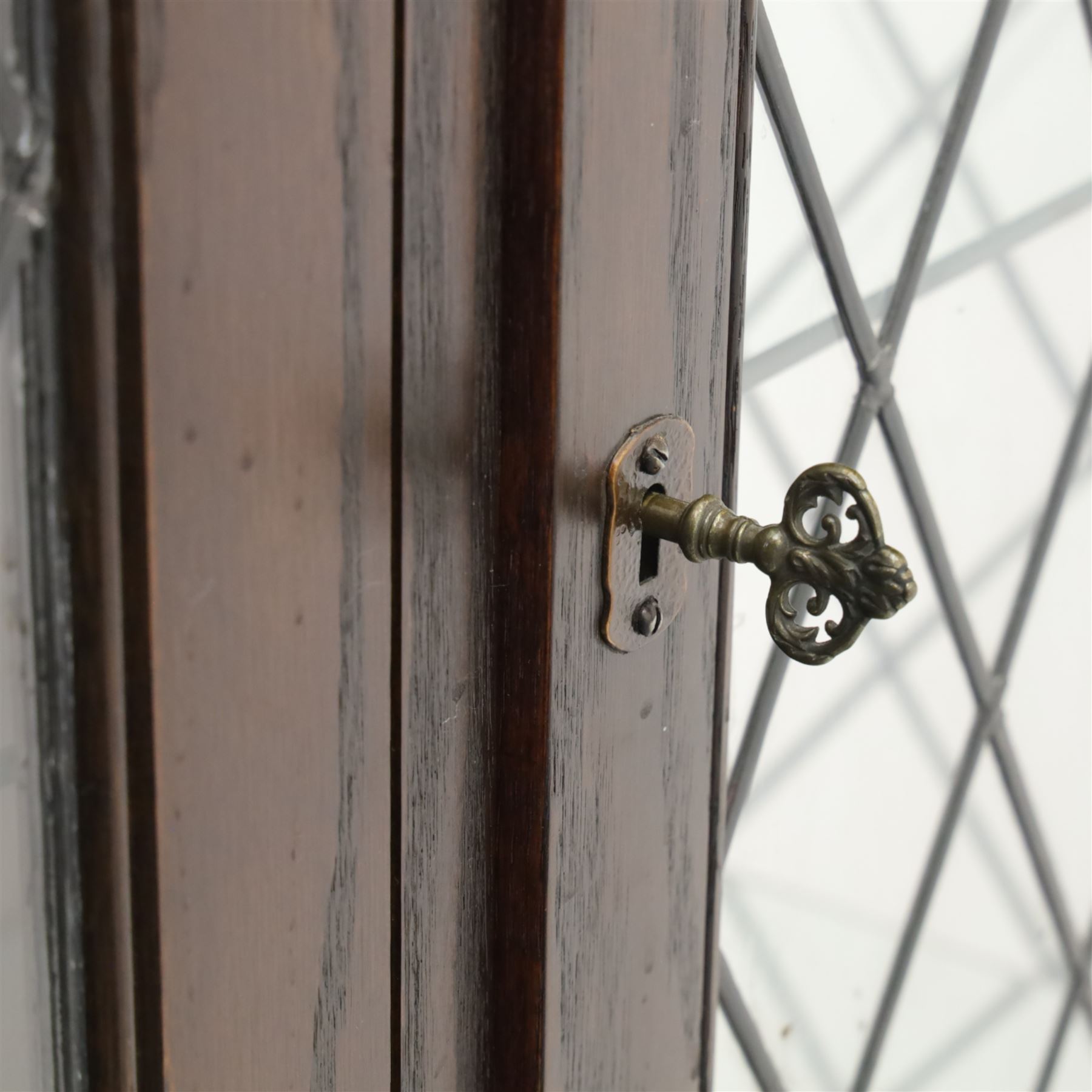 Mid 20th century oak display cabinet, the moulded rectangular cornice above a pair of leaded glazed doors with diamond lattice glazing, enclosing adjustable shelving, the lower section fitted with four short drawers with brass ring handles, flanked by chamfered uprights with carved leaf detail