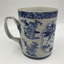 Two large 18th century Chinese blue and white tankards, each of cylindrical form, the first example with foliate mounted strap handle, the body painted with a shaped panel depicting a riverside landscape with pagodas and pine trees, against a textured ground decorated with floral sprays, H15cm D12cm, the second with serpent handle, the body painted with a similar riverside landscape, H14cm D12cm