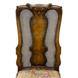 Pair of early 20th century Queen Anne design chairs, the cresting rail carved with scroll and central shell motif, shaped uprights and splat encased in cane work panels, shaped moulded seat frame with shell motif, floral needlework upholstered drop-in seat cushion, on shell carved cabriole supports with ball and claw feet, united by turned and shaped middle stretcher carved with acanthus leaf