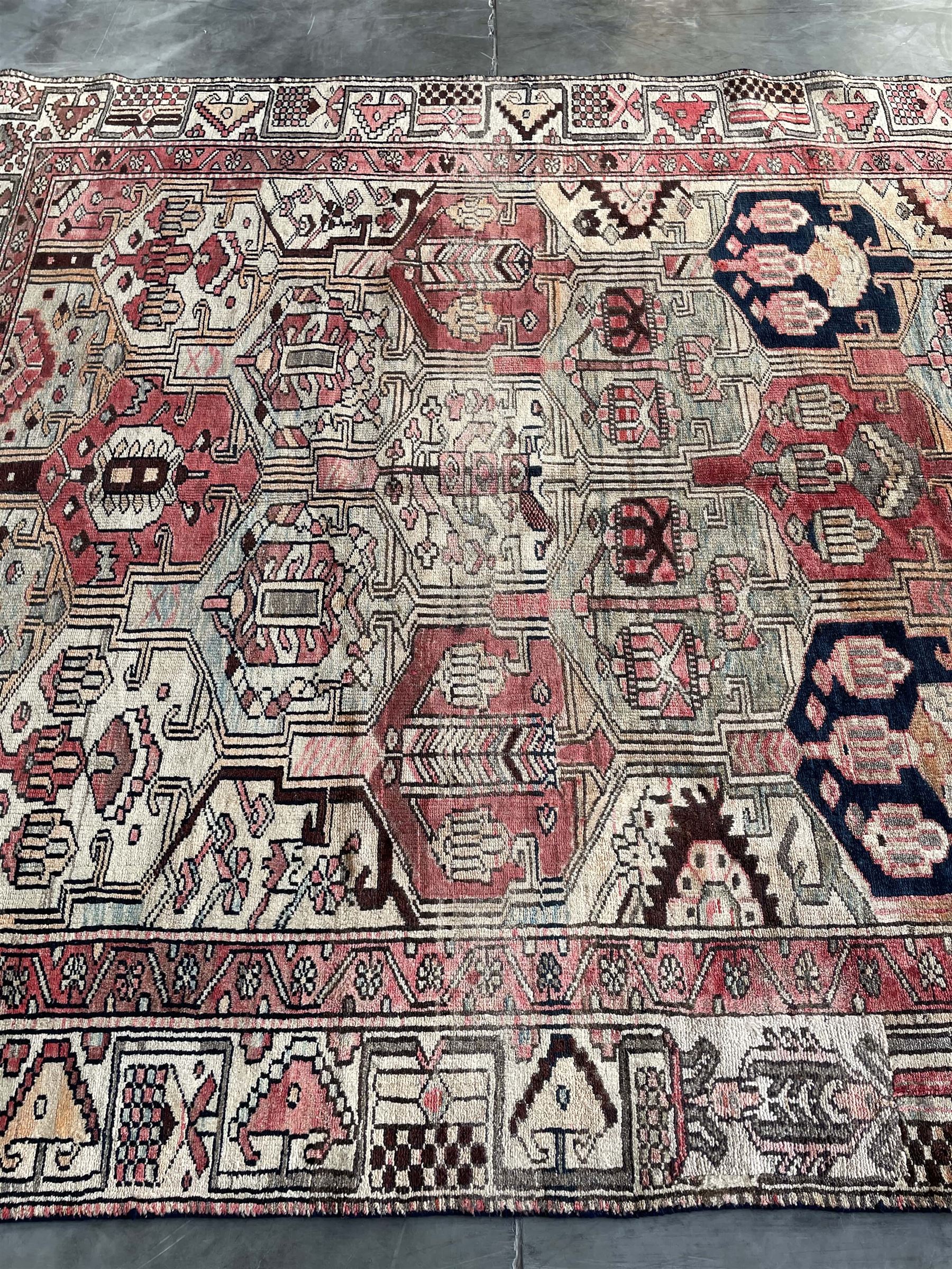 Persian Heriz red and pale ground rug, depicting multiple shaped panels with stylised motifs and designs, geometric patterned border