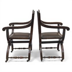 Late 20th century stained beech Savonarola chair, the carved crest rail and open arms above an upholstered leather seat, raised on an X framed base with carved foliate and mask decoration, joined by turned stretcher and ending in castors
