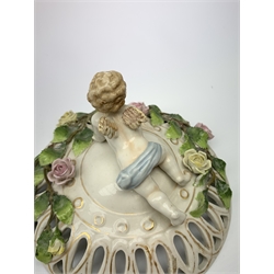 A Schierholz porcelain pot pourri basket and cover, c.1900, the pierced body raised upon three scroll feet, encrusted with vines and flowers and surmounted by a cherub with harp, with printed mark beneath, H21cm, together with another similar smaller Schierholz example. (2). 
