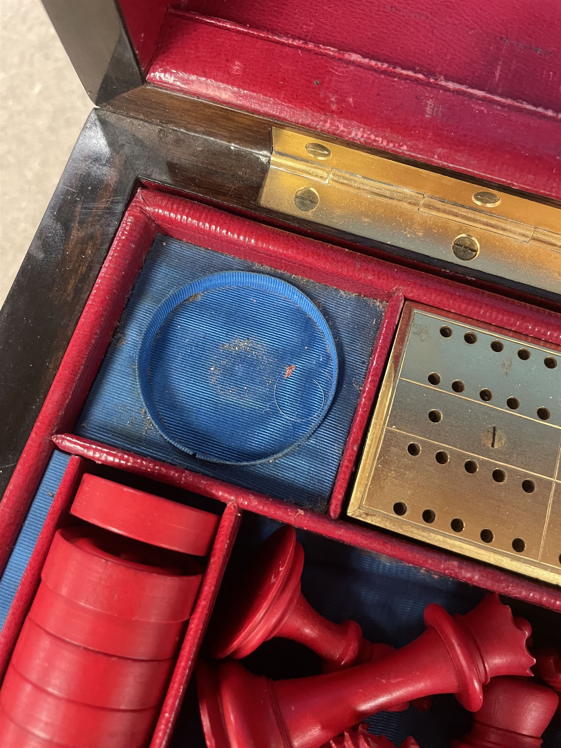 19th century walnut and brass bound games compendium box, painted to enhance the grain, of rectangular form, the hinged opening cover with rounded sides, central brass cartouche with engraved lion crest, and brass riveted straps, opening to reveal a red leather and blue silk lined compartmented interior, with fold-down games board, and lift-out tray containing playing cards, ebony turned dice towers, white and red stained bone draughts, and chess pieces, ivory dice, and ivory and ebony whist markers, and brass bezique board, cribbage board and markers, H15cm W32cm D24cm
This lot has been registered for sale under Section 10 of the APHA Ivory Act