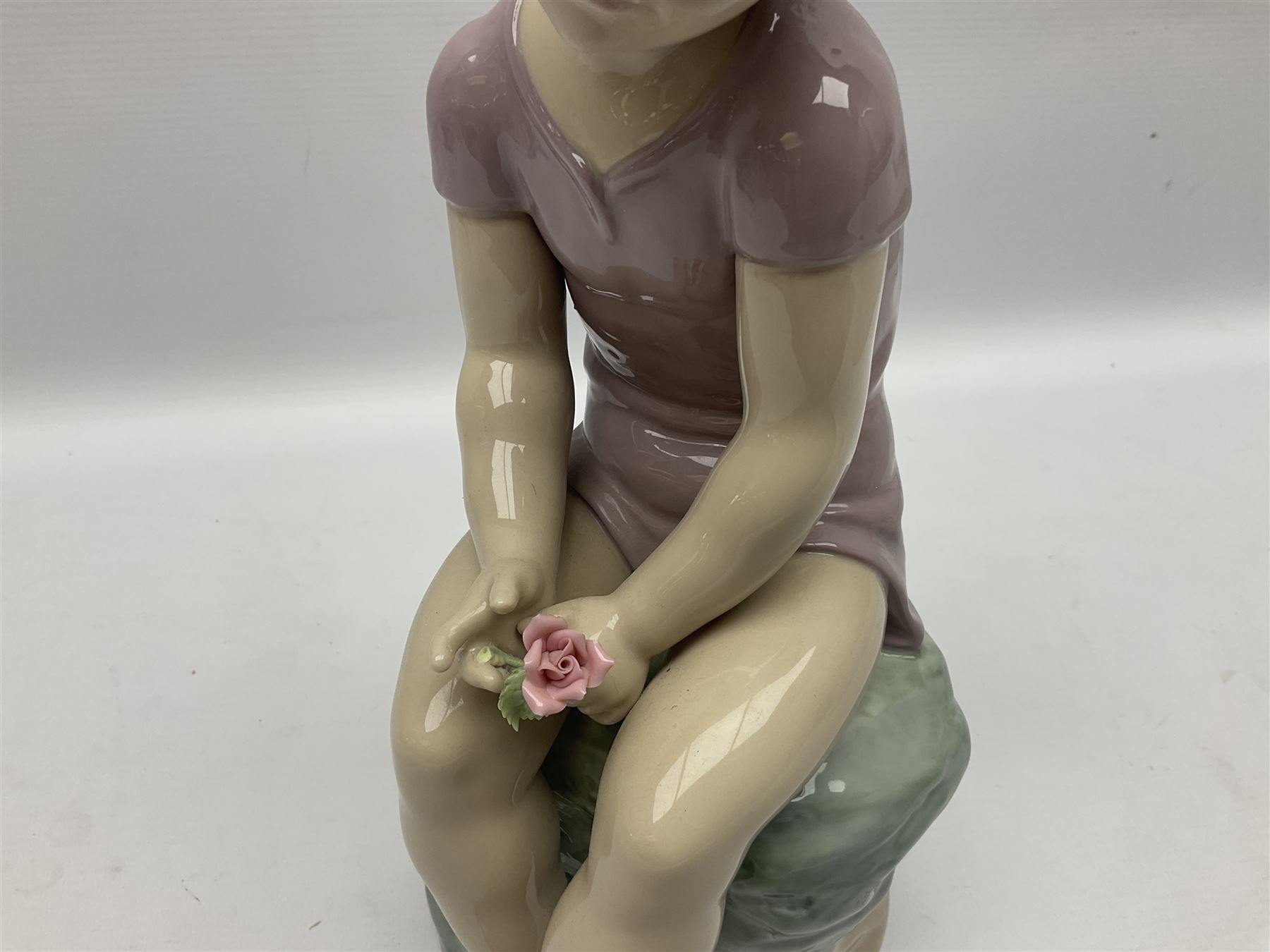 Large Nao figure modelled as a young girl seated upon a rock holding a rose, H30cm