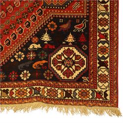 Persian Shiraz rug, hand-knotted tribal rug, bold geometric central medallion, set within a large hexagonal crimson field with angular stepped corners in dark blue, with boteh motifs, rosettes, and other tribal symbols arranged in diagonal rows, the corners with indigo spandrels decorated with zoomorphic and arboreal motifs, main border composed of a floral meander motif with large rosette, flanked guard borders with vine and leaf motifs 