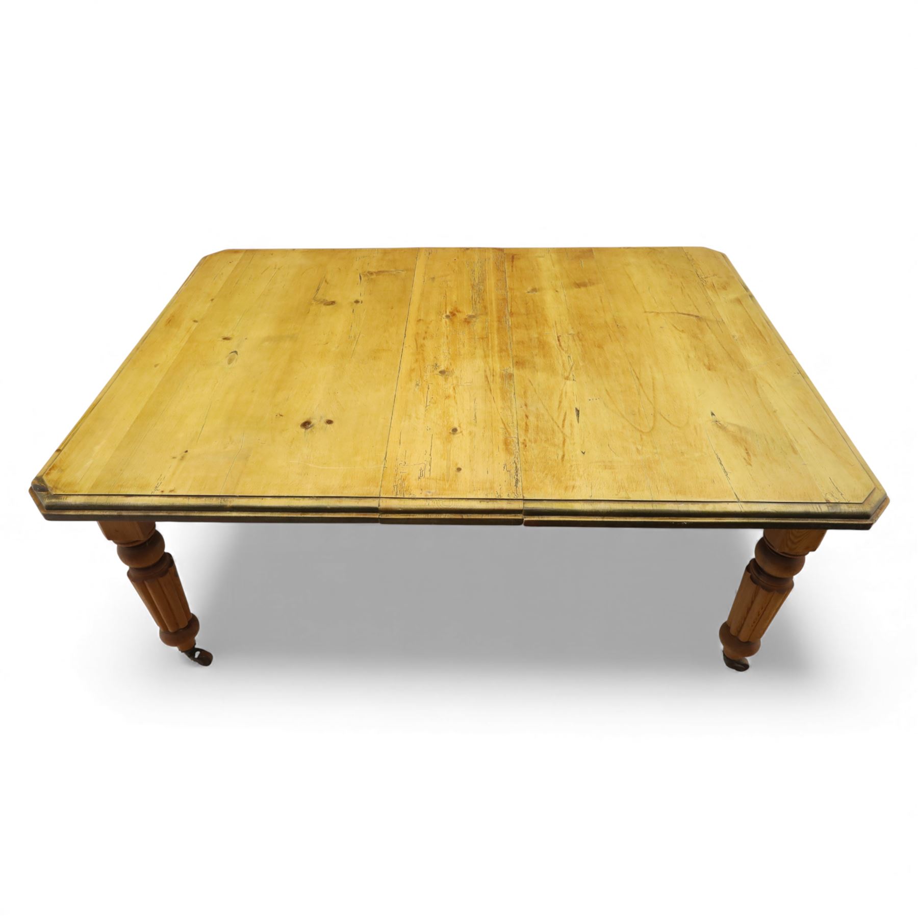 Early 20th century stripped pine kitchen table, the rectangular planked top with moulded edge and canted corners, upon stained pine turned and fluted legs with castors