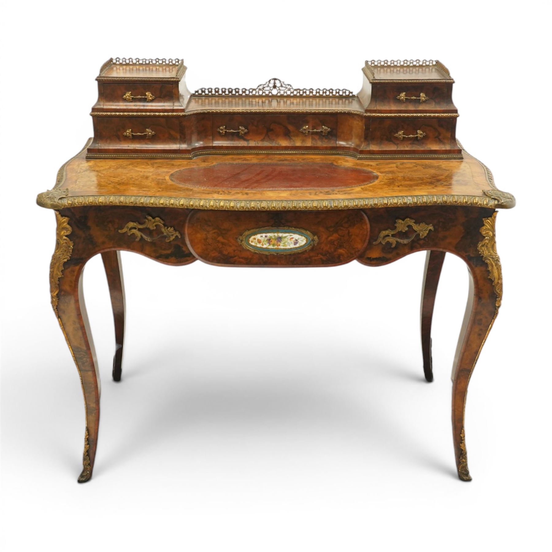 Victorian figured walnut and kingwood-banded ladies writing table, the raised superstructure with three-quarter pierced brass raised gallery back, fitted with five assorted drawers, the serpentine shaped top with oval inset leather surface, the bronze edge of egg and dart form with cartouche corners, fitted with central frieze drawer with inset Sevres-style floral ceramic plaque, raised on cabriole supports with gilt metal mounts