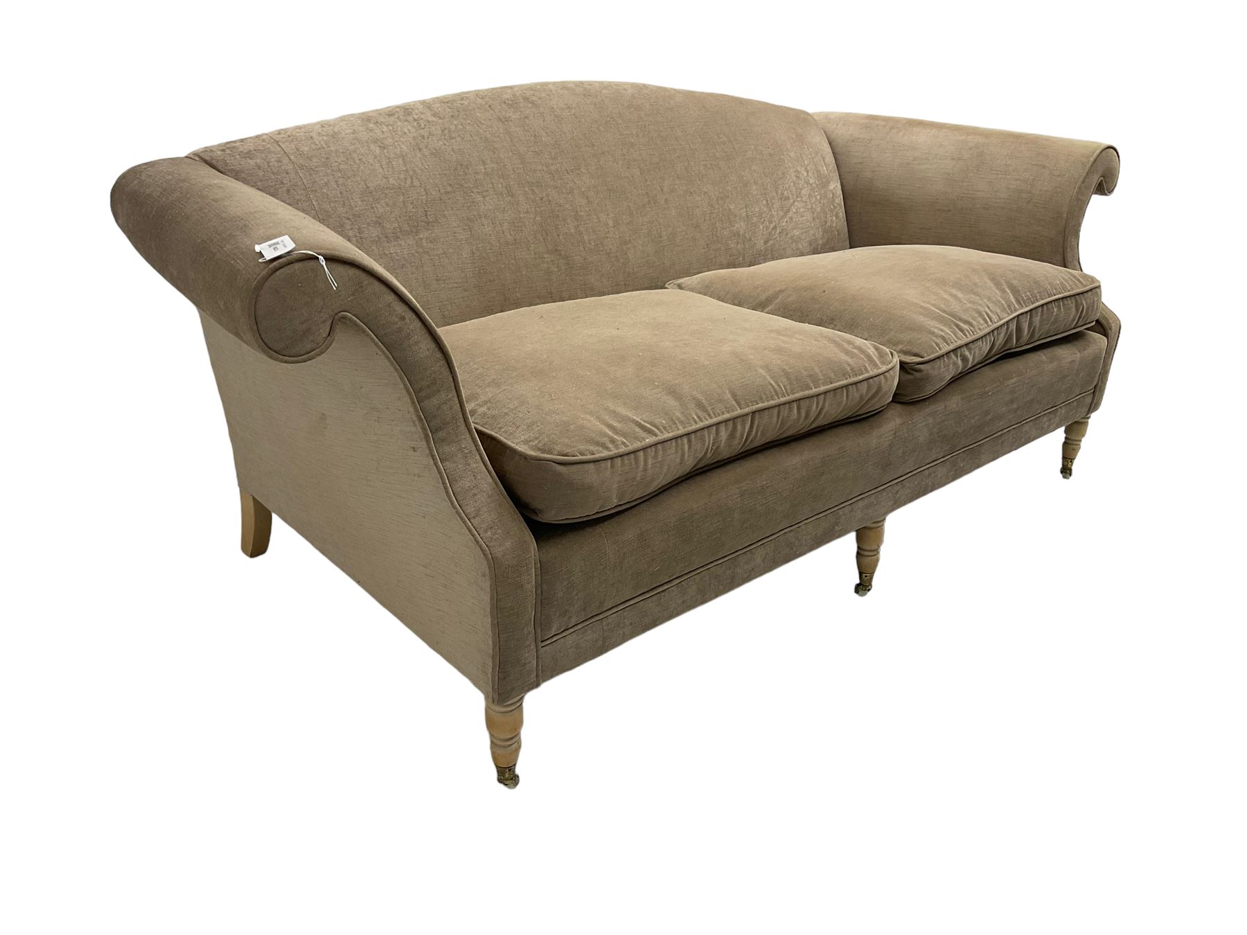 Traditional three seat sofa, curved back over scrolled arms, upholstered in crushed beige fabric with matching loose cushions, on turned front supports with brass and ceramic castors, together with matching footstool