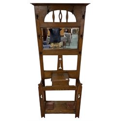 Arts & Crafts period oak hall stand, projecting moulded cornice over arched cut-out decorated with shaped vertical rails, fitted with rectangular bevelled mirror back over hinged glove compartment, on straight pierced supports with shaped pediments 