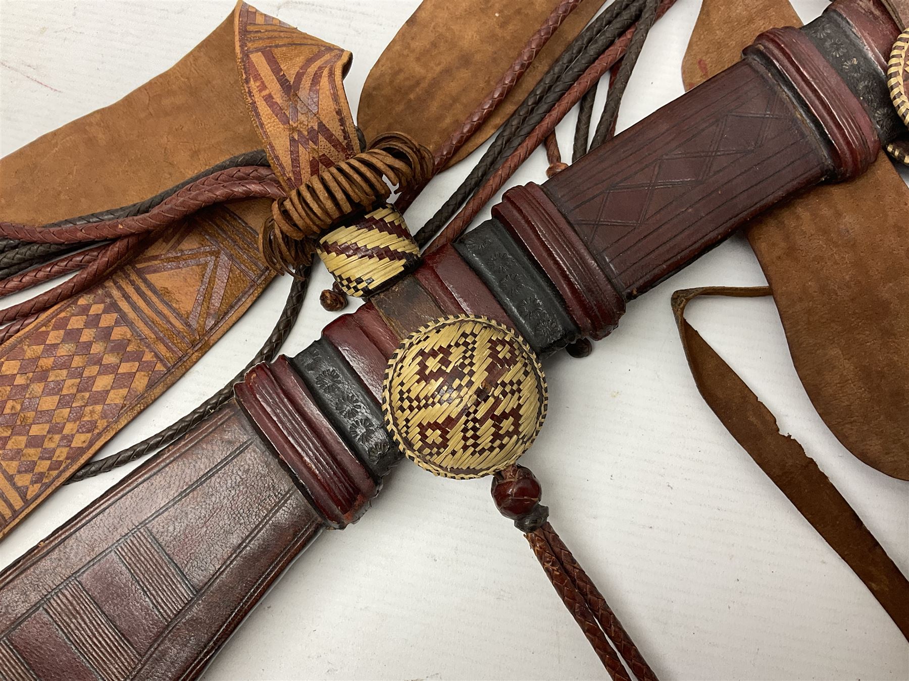 Mandingo sword with 63cm plain curving steel blade and leather covered grip with white metal ribbed spherical pommel; in decorative leather leaf scabbard with plaited tassels and shoulder strap L78cm overall