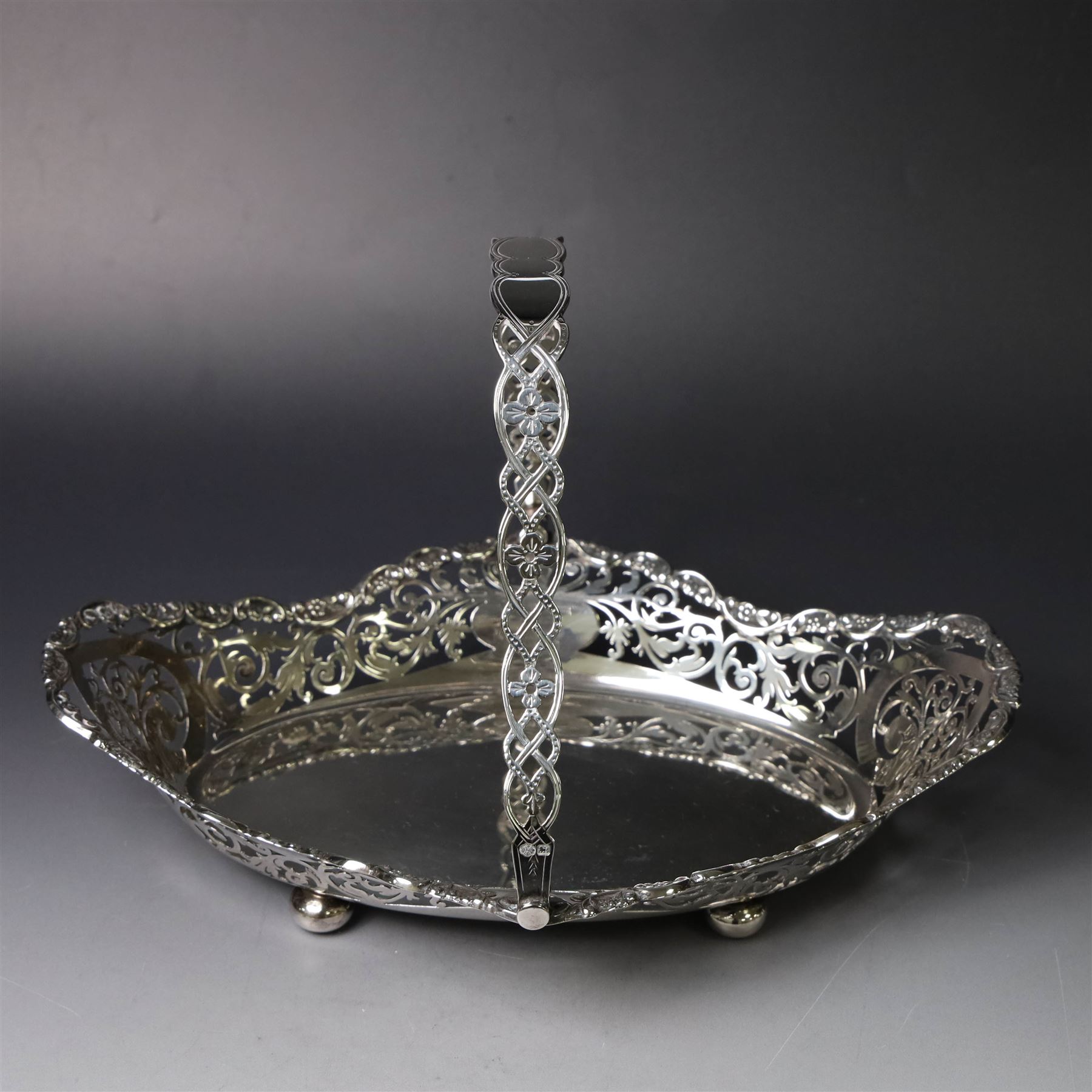 Early 20th century swing handled basket, of oval form with pierced sides and floral C scroll rim, upon four bun feet, hallmarked William Hutton & Sons Ltd, Sheffield 1915, widest point W29cm