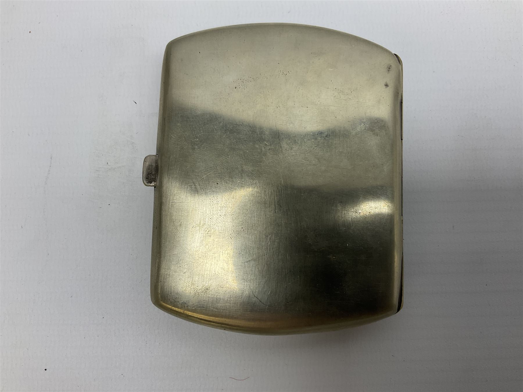 Early 20th century Continental erotic cigarette case, the silver-plate body of curved rectangular form with cover decorated with painted enamel street scene depicting young boy in squatting position lighting a cigarette shielded from the wind by his girlfriend, who is lifting the skirt of her dress up over him, with gilt interior, L9cm