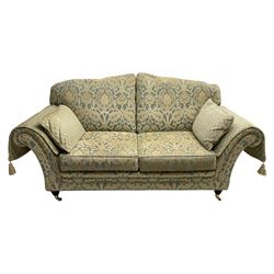Traditional shape two seat sofa, upholstered in repeating foliate pattern fabric, with side cushions and arm covers, on turned feet with brass cups and castors