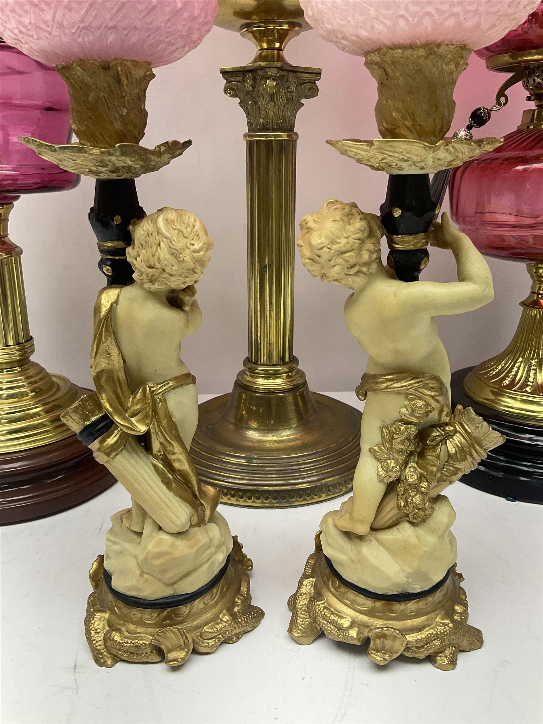 Victorian cast brass oil lamp, with fluted pink glass shade, together with two smaller brass oil lamps with pink shades and reservoirs and a pair of oil lamps, the bases modelled as putti, with pink glass reservoir  and frosted shades, tallest H70cm