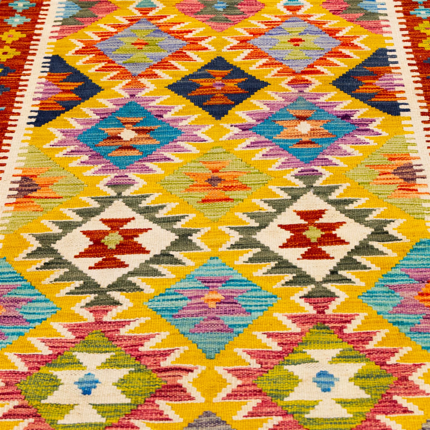Afghan Chobi kilim flatweave runner with a repeating stepped diamond medallion design in live green, sky blue, rust, teal, purple, and ivory, framed by geometric borders in tones of orange and crimson