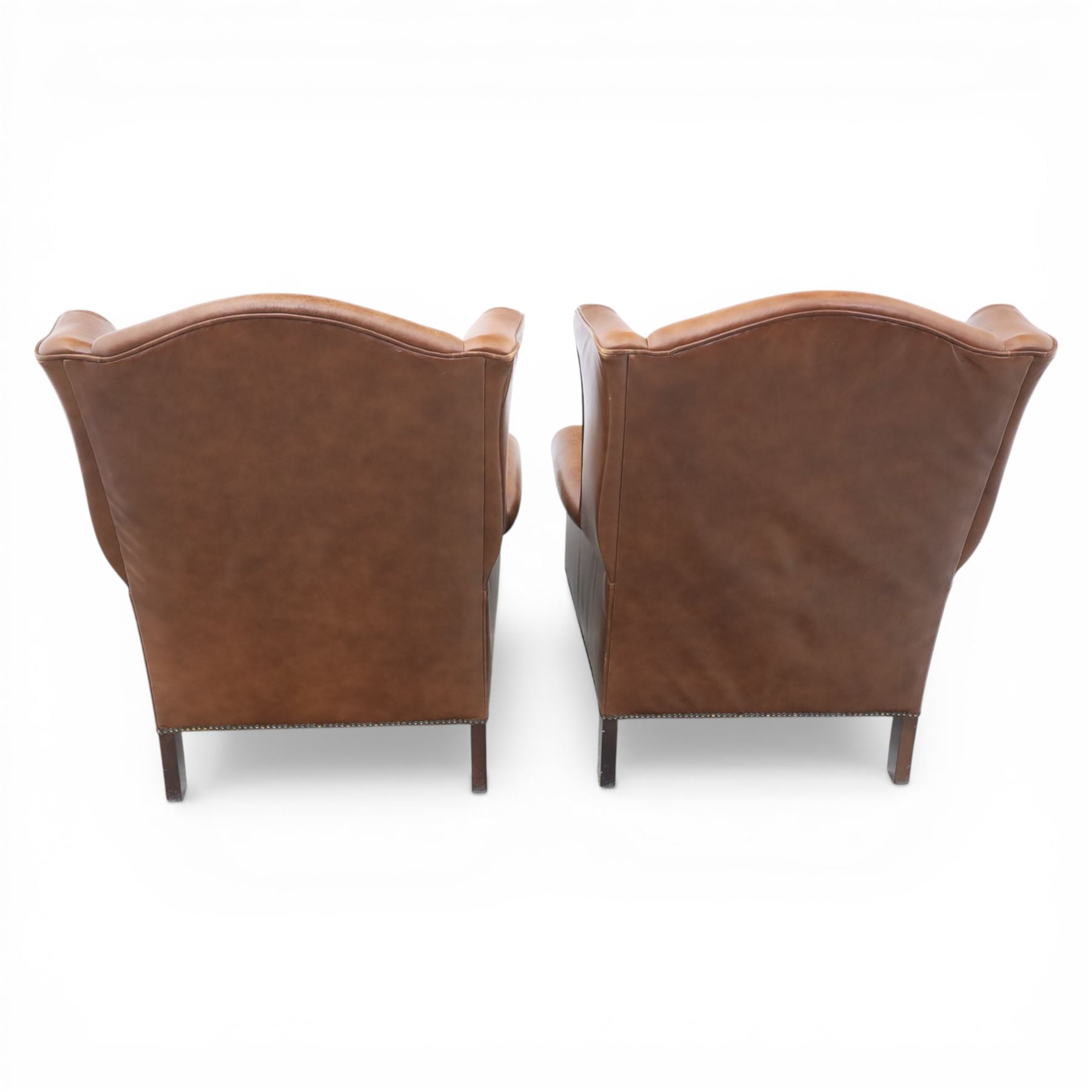 Laura Ashley - Pair of brown leather wingback armchairs, with scrolled arms and loose cushion seat, brass studded trim, on cylindrical tapering legs terminating in castors