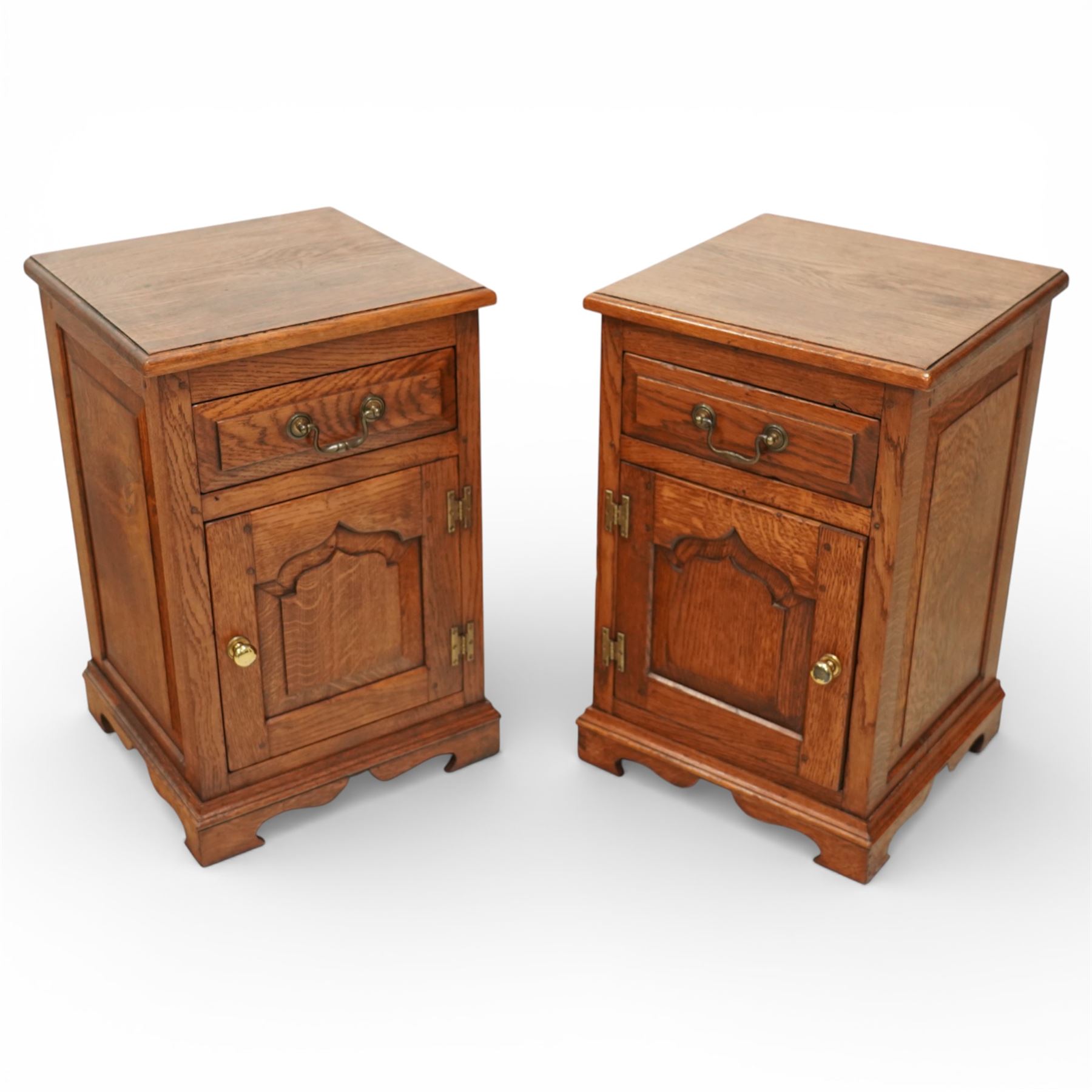 20th century pair of oak bed side cabinets, in the manner of Titchmarsh & Goodwin, plain rectangular tops over drawers fitted with brass handles and cupboard doors with carved arched panels, panelled sides and backs, raised on shaped bracket feet