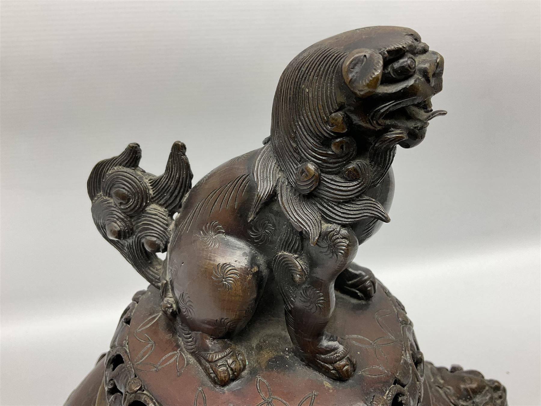 Japanese bronzed koro, the body of globular form with twin cast zoomorphic mask handles, decorated in relief with birds upon blossoming branches, against a ground incised with rushes and peonies, the flat toped domed cover with pierced band and surmounted by a cast figure of a Foo dog, the whole upon three zoomorphic mask feet, with impressed character type mark beneath, H35.5cm